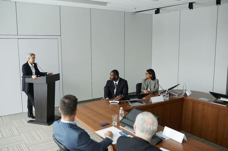 Diverse group of professionals in a formal conference room with a speaker at the podium